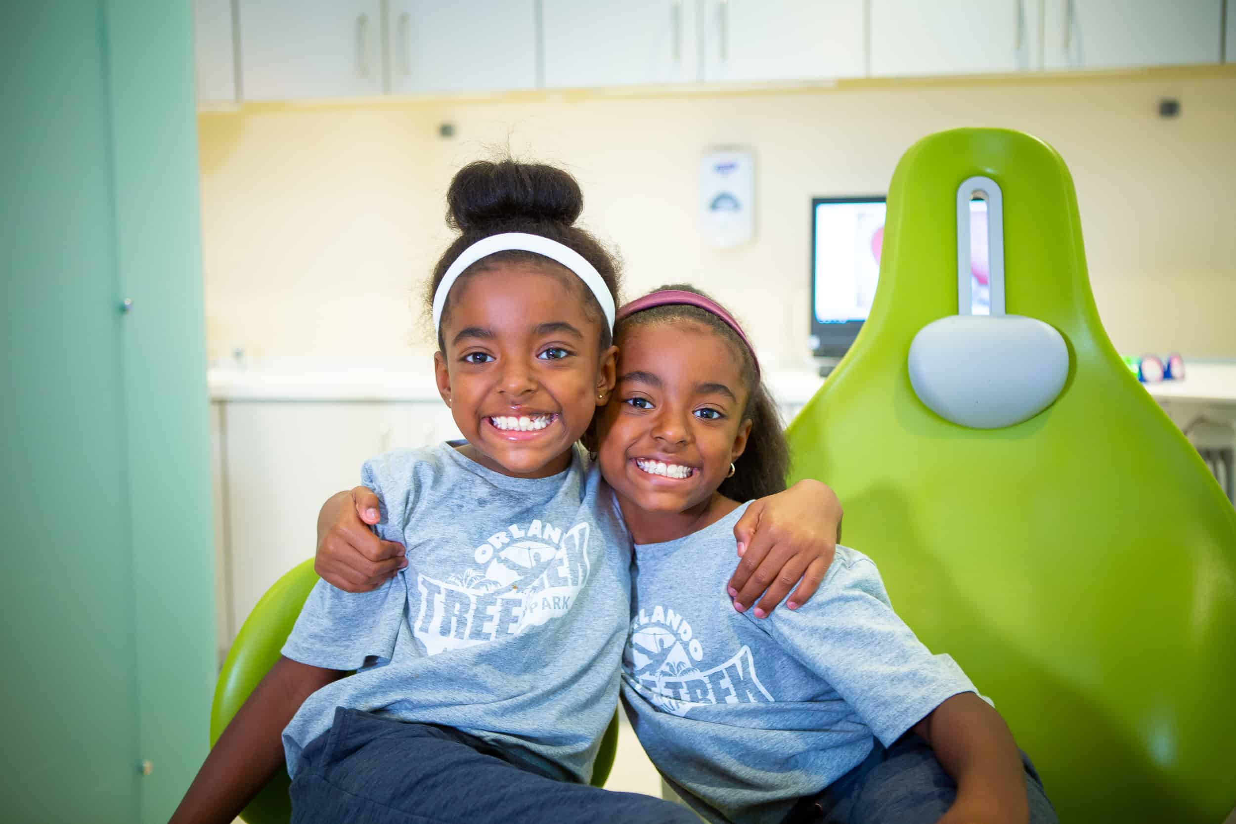 two children hugging and smiling at the dentist office sitting in a chair