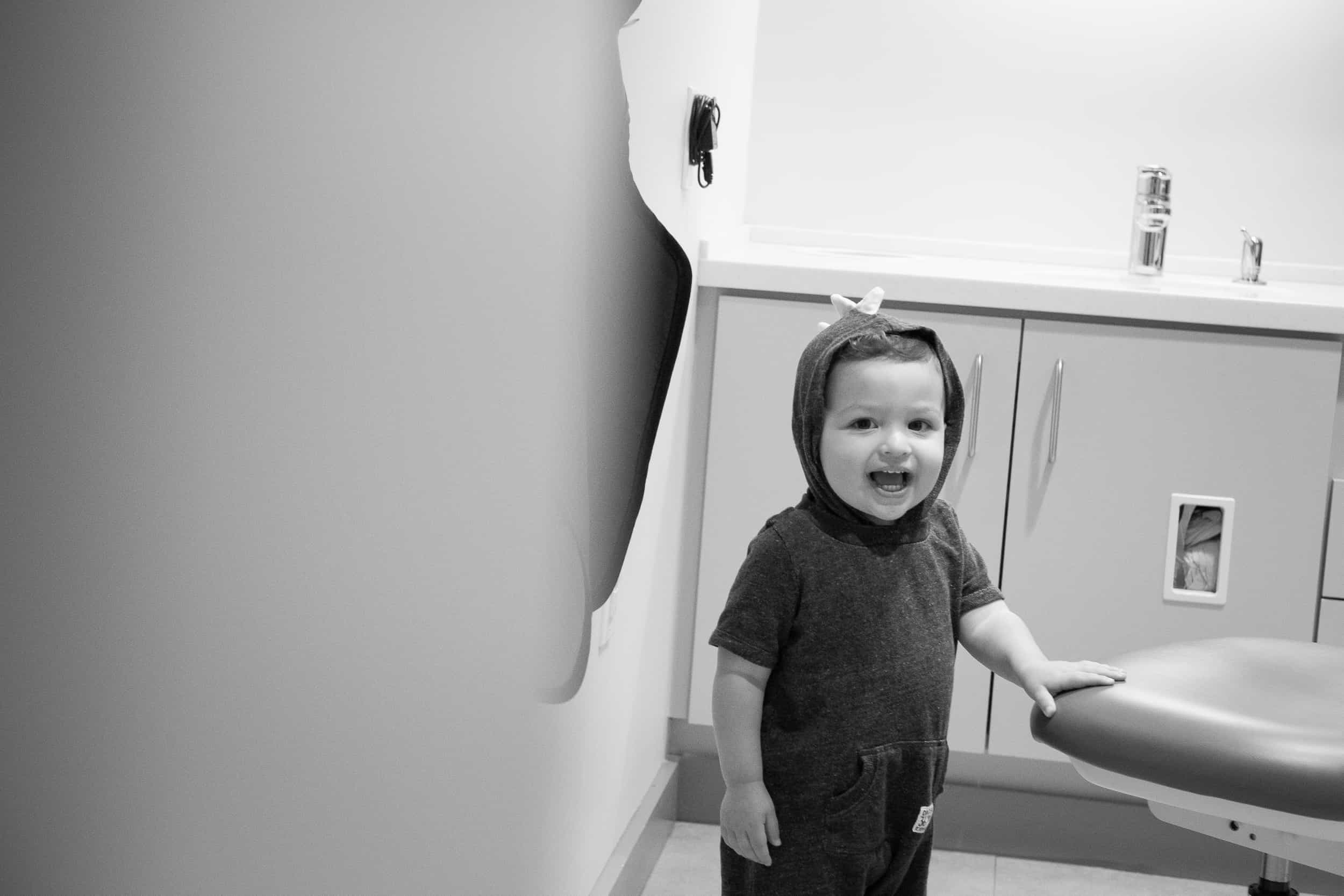 small child smiling at the dentist wearing a dinosaur costume.